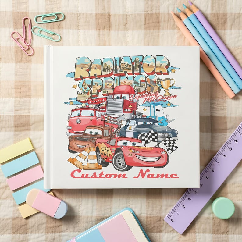 Puede incluir: Un libro de tapa dura blanco con una colorida ilustraci&oacute;n de personajes de la pel&iacute;cula Cars, incluyendo a Rayo McQueen y Mate. El t&iacute;tulo "Radiator Springs" se muestra en una fuente estilizada, con las palabras "Custom Name" debajo.