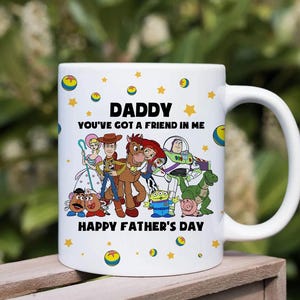 Puede incluir: Taza de cer&aacute;mica blanca con una ilustraci&oacute;n de personajes de dibujos animados. La taza tiene el texto "DADDY YOU'VE GOT A FRIEND IN ME" y "HAPPY FATHER'S DAY". El dise&ntilde;o incluye estrellas amarillas y c&iacute;rculos.