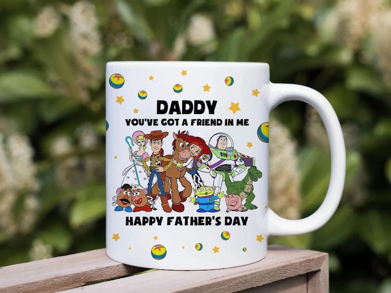 Puede incluir: Taza de cer&aacute;mica blanca con una ilustraci&oacute;n de personajes de dibujos animados. La taza tiene el texto "DADDY YOU'VE GOT A FRIEND IN ME" y "HAPPY FATHER'S DAY". El dise&ntilde;o incluye estrellas amarillas y c&iacute;rculos.