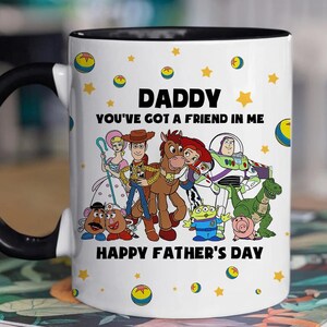 Puede incluir: Taza de cer&aacute;mica blanca con interior y asa negros. La taza presenta un gr&aacute;fico colorido de personajes de la pel&iacute;cula Toy Story, con el texto "DADDY YOU'VE GOT A FRIEND IN ME HAPPY FATHER'S DAY". Estrellas amarillas y gr&aacute;ficos de bolas de Toy Story est&aacute;n dispersos alrededor de la taza.