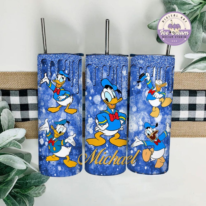 May include: Three blue and white tumbler cups with a glitter finish. Each cup features a different image of Donald Duck in a sailor outfit. The middle cup has the name "Michael" written in gold lettering.