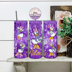 May include: Three purple and gold glitter tumblers with a design of Daisy Duck in different poses. The tumblers have a dripping glitter effect and the middle tumbler has the name "Patricia" written on it.