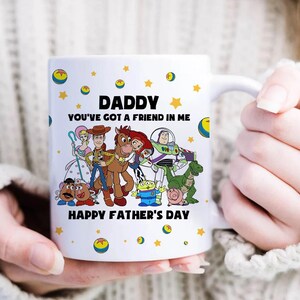 Puede incluir: Taza de cer&aacute;mica blanca con personajes de dibujos animados y el texto "DADDY YOU'VE GOT A FRIEND IN ME HAPPY FATHER'S DAY". La taza est&aacute; decorada con estrellas y planetas amarillos.