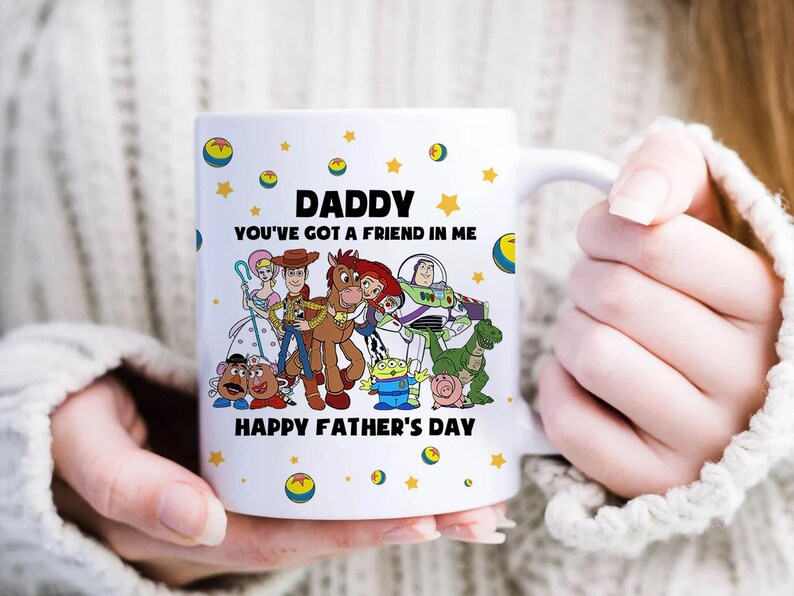 Puede incluir: Taza de cer&aacute;mica blanca con personajes de dibujos animados y el texto "DADDY YOU'VE GOT A FRIEND IN ME HAPPY FATHER'S DAY". La taza est&aacute; decorada con estrellas y planetas amarillos.