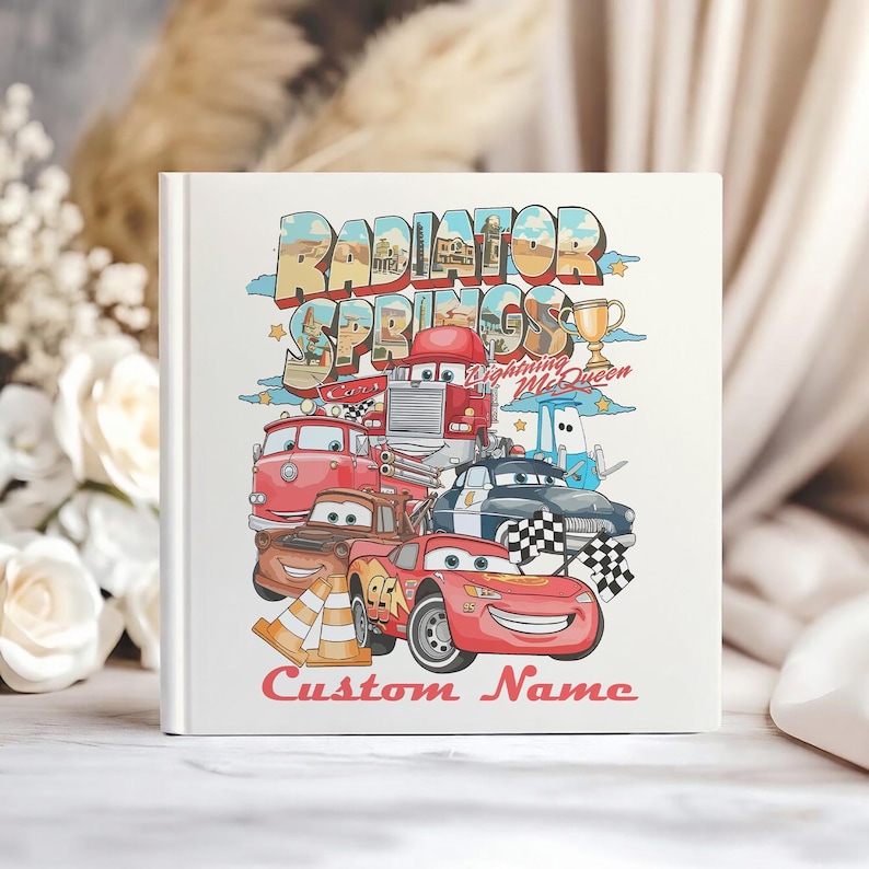 Puede incluir: Un libro cuadrado blanco con una colorida ilustraci&oacute;n de personajes de la pel&iacute;cula Cars. La portada presenta el texto "Radiator Springs" y "Lightning McQueen", junto con las palabras "Custom Name" en rojo.