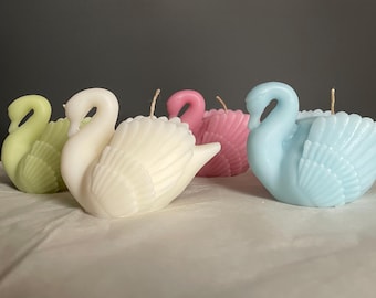 May include: Four swan-shaped candles in different colors: green, white, pink, and blue. The candles are made of wax and have a detailed design.