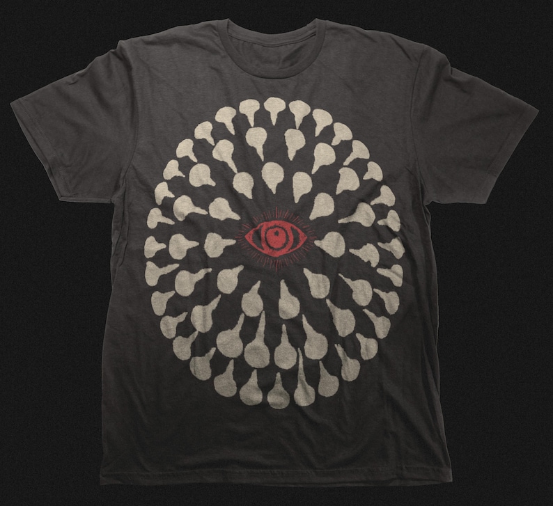 May include: Dark gray t-shirt featuring a circular design of white teardrop shapes surrounding a red eye. The graphic is centered on the front of the shirt. The shirt is made of a soft material.