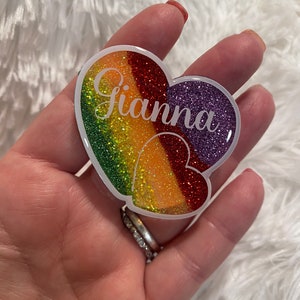 May include: A white heart-shaped resin ornament with a rainbow glitter design and the name "Gianna" written in white.