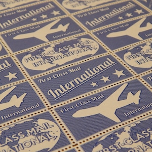 May include: A close-up of a sheet of postage stamps with a blue and white design. The stamps feature an airplane and the text "First-Class Mail International".