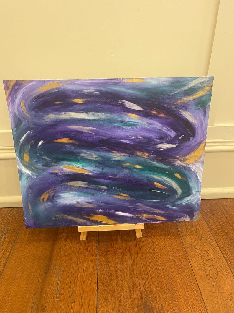 Puede incluir: Pintura abstracta sobre lienzo con trazos en espiral de pintura p&uacute;rpura, turquesa, dorada y blanca. La pintura se muestra en un peque&ntilde;o caballete de madera.