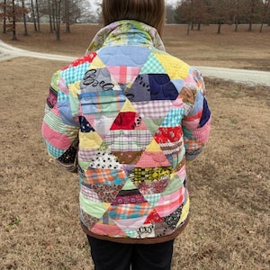 May include: A colorful patchwork jacket with a variety of fabric patterns and colors, including pink, blue, yellow, and red. The jacket has a brown collar and trim. The back of the jacket is visible.