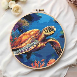 May include: A colorful cross-stitch embroidery of a sea turtle swimming in a blue ocean with coral reefs and fish. The turtle is orange, yellow, and brown with a green shell.