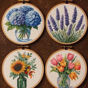 Peut inclure: Modèles PDF de point de croix avec des motifs floraux. L'image présente quatre cerceaux de point de croix avec des compositions florales détaillées : hortensias bleus, lavande violette, un tournesol et des tulipes colorées. Le texte "CROSS STITCH PDF PATTERNS" est en haut.