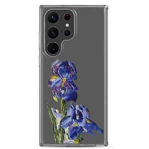 Peut inclure: Une coque de téléphone transparente avec une image peinte de deux fleurs d'iris bleues sur un fond gris. La coque a un renflement de caméra surélevé avec trois objectifs.