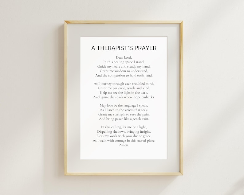 May include: A framed print featuring the text "A Therapist's Prayer" in a black, elegant font. The print is set against a white background and enclosed in a light-colored wooden frame, suitable for a counseling office or home decor.