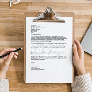 Puede incluir: Una carta blanca en un portapapeles con un bol&iacute;grafo negro sobre una mesa de madera. La carta es una nota de un profesional de la salud mental a un arrendador solicitando adaptaciones razonables para un inquilino.