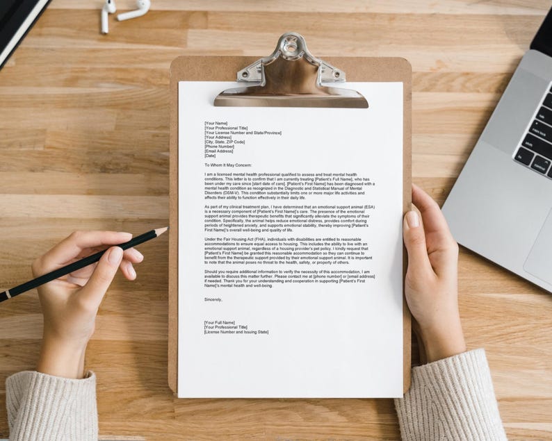 Puede incluir: Una carta blanca en un portapapeles con un bol&iacute;grafo negro sobre una mesa de madera. La carta es una nota de un profesional de la salud mental a un arrendador solicitando adaptaciones razonables para un inquilino.