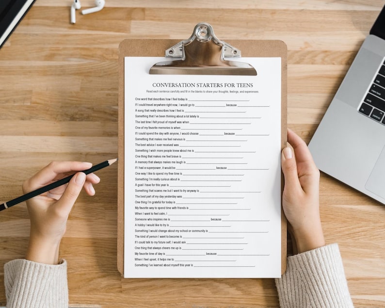 K&ouml;nnte beinhalten: Ein Klemmbrett mit einem Arbeitsblatt mit der Aufschrift "Conversation Starters for Teens". Eine Person h&auml;lt das Klemmbrett und einen Bleistift. Ein Laptop und Kopfh&ouml;rer sind im Hintergrund zu sehen. Das Arbeitsblatt enth&auml;lt L&uuml;ckentexte.