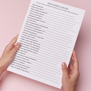 May include: A white paper titled "PROCESSING ANGER" is held by hands against a pink background. The paper contains fill-in-the-blank prompts about anger, with lines for responses. The text is in black.