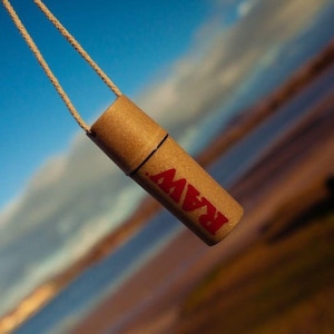 May include: A brown cardboard tube with a string attached to it. The tube has the word "RAW" printed on it in red letters.