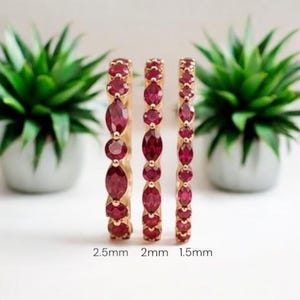 May include: Three gold rings set with deep red faceted gemstones in alternating round and marquise shapes. The rings are labeled with widths of 2.5mm, 2mm, and 1.5mm, showing the variation in stone size and band thickness across the three pieces.
