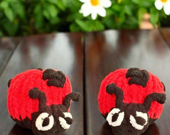 May include: Two red and black ladybug plush toys with white eyes. The ladybugs are sitting on a wooden table.