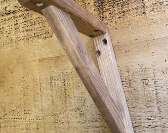 May include: A wooden shelf bracket with a triangular shape and a natural wood finish. The bracket has three screw holes on each side.
