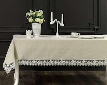 May include: A white tablecloth with a lace trim, a white candle holder, a white vase with white flowers, and two white candle holders on a wooden table.