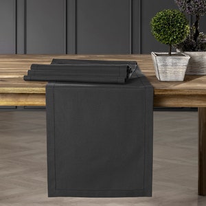 Könnte beinhalten: Ein dunkelgrauer Tischläufer mit dezentem Glanz, in der Mitte gefaltet und auf einem Holztisch platziert. Der Läufer ist etwa 35 cm breit und 178 cm lang.