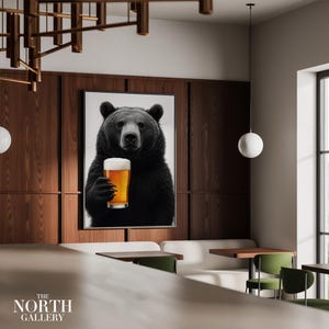 May include: A framed art print depicting a black bear raising a pint of beer. The bear is the central figure, set against a neutral backdrop. The print is mounted on a dark wood panelled wall. The North Gallery logo is visible.