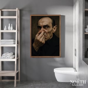 Könnte beinhalten: Ein gerahmtes Porträt eines Mannes, der sich die Nase zuhält, in einem modernen Badezimmer. Der Mann trägt einen schwarzen Mantel. Das Badezimmer hat eine weiße Toilette, graue Wände und ein Holzregal mit Handtüchern und dekorativen Flaschen. Das Logo The North Gallery ist sichtbar.