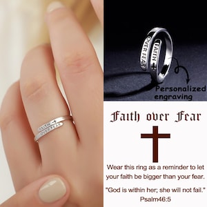 May include: A silver ring with the words "FAITH" and "OVER FEAR" engraved on it. The ring has a cross symbol and is shown on a finger. The image also includes the text "Faith over Fear" and a cross symbol.