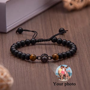 May include: Black beaded bracelet with a central metal piece and two tiger eye beads. The bracelet has an adjustable black cord closure. A small photo is visible in the lower right corner with the text "Your photo".