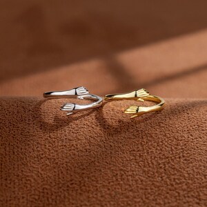May include: Two silver rings with a design of two hands reaching out to each other. One ring is gold and the other is silver.