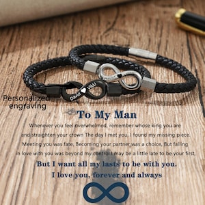 May include: Two black leather bracelets with infinity symbols and the names "David" and "Vikki" engraved on them. The bracelets are on a wooden surface with the text "To My Man" and a love message.