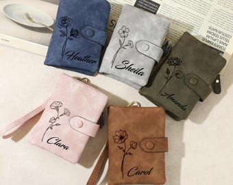Può includere: Cinque portafogli personalizzati in similpelle con motivi floreali e nomi ricamati. I portafogli sono di diversi colori: blu, grigio, verde, rosa e marrone.