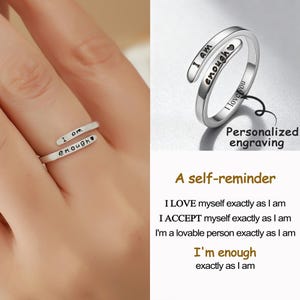 May include: A silver-colored wrap ring with the words "I am enough" engraved on it. The ring is shown on a hand, with a second image of the ring with the words "I love you" and "Personalized engraving". The image also includes the text "A self-reminder".
