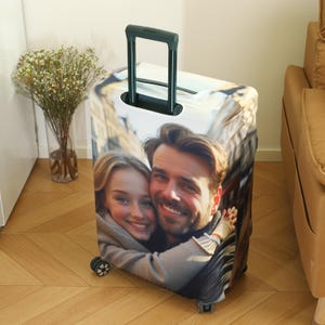 May include: A luggage cover with a photo of a couple smiling at the camera. The couple is wearing casual clothing and is standing in a city street. The luggage cover is black and has a zipper closure.