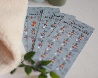 May include: A set of four blue and white cards with a dinosaur theme. The cards have the text "Dino €2 SPAAR CHALLENGE" and feature illustrations of dinosaurs.