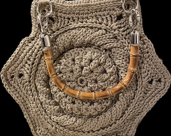 Könnte beinhalten: Eine gehäkelte Handtasche mit einem braunen Bambusgriff. Die Tasche ist aus beigefarbenem Häkelmaterial gefertigt und hat ein Sternmuster.