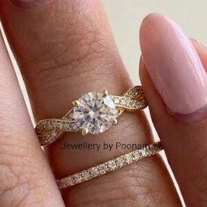 May include: A gold engagement ring featuring a round brilliant-cut center stone with a twisted band design, paired with a thin gold eternity band encrusted with small clear stones. The text Jewellery by Poonam is visible on the ring.