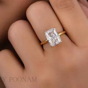 May include: A gold ring featuring a large, clear, rectangular-shaped diamond. The ring is worn on a person's finger.