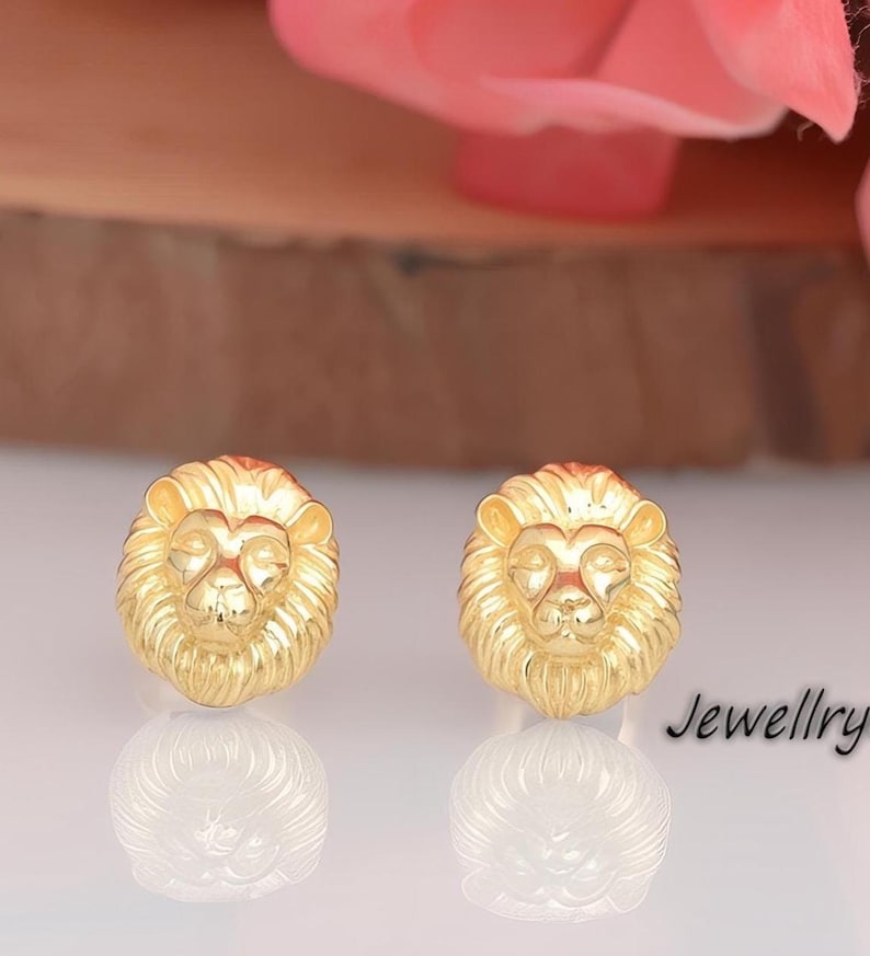 May include: A pair of gold lion head stud earrings. The earrings are made of a shiny gold metal and feature a detailed lion head design.