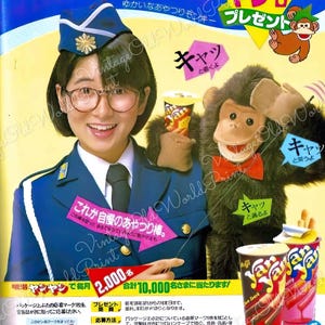 May include: A colorful Japanese advertisement for Yan Yan snack crackers. The ad features a woman in a blue uniform holding a monkey puppet. The text on the ad says "Yan Yan" and "New Release".