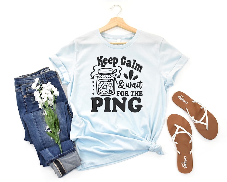 May include: Light blue t-shirt with a black graphic that says "Keep Calm & wait for the PING" with a jar of pickles illustration.