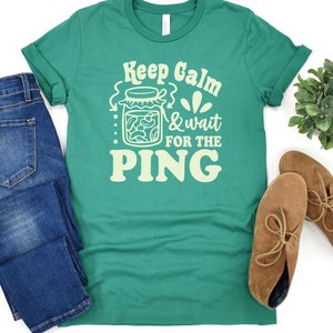 May include: A green t-shirt with a white graphic design that says "Keep Calm & Wait for the Ping" with a jar of pickles in the design.