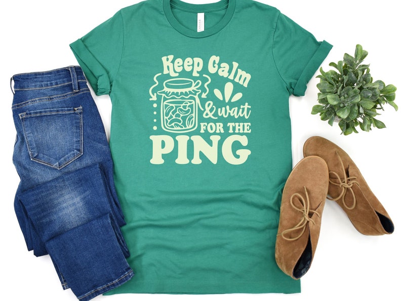 May include: A green t-shirt with a white graphic design that says "Keep Calm & Wait for the Ping" with a jar of pickles in the design.