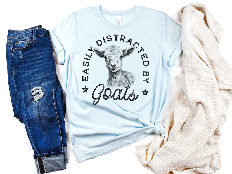 May include: Light blue t-shirt with a black and white graphic of a goat and the text "Easily Distracted By Goats".