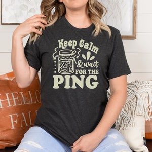 May include: A dark gray t-shirt with the text "Keep Calm & wait for the PING" in a light yellow color. The text is surrounded by a graphic of a jar of pickles.