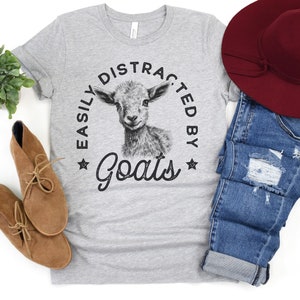 May include: A gray t-shirt with a black and white illustration of a goat and the text "Easily Distracted by Goats".